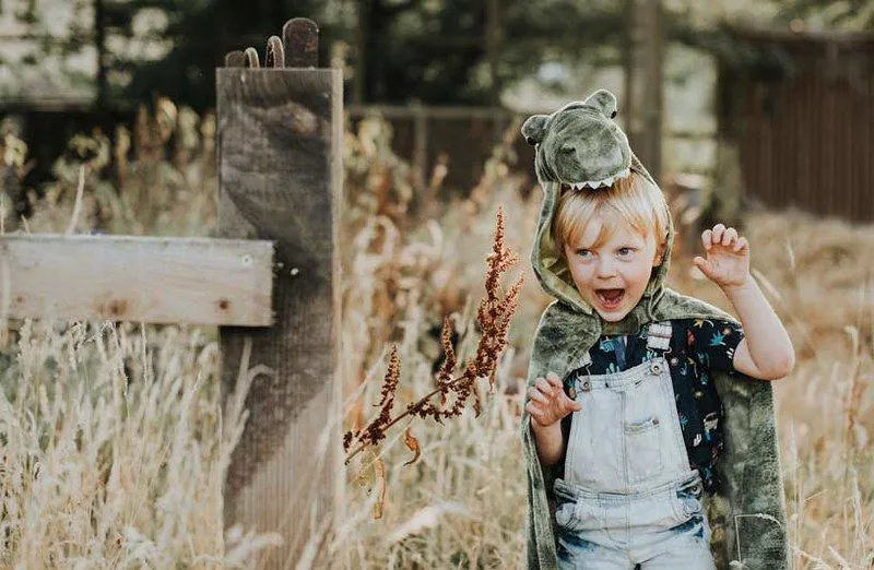 little boy in dinosaur suit running in the fields