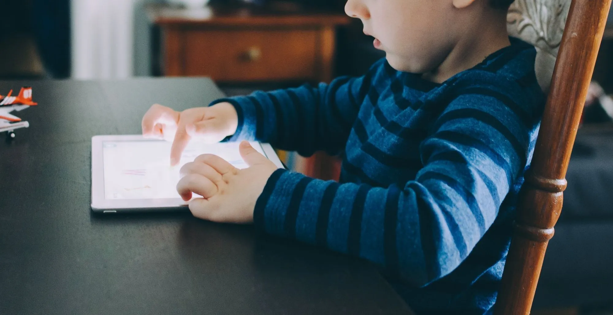 young boy sat at table playing on tablet