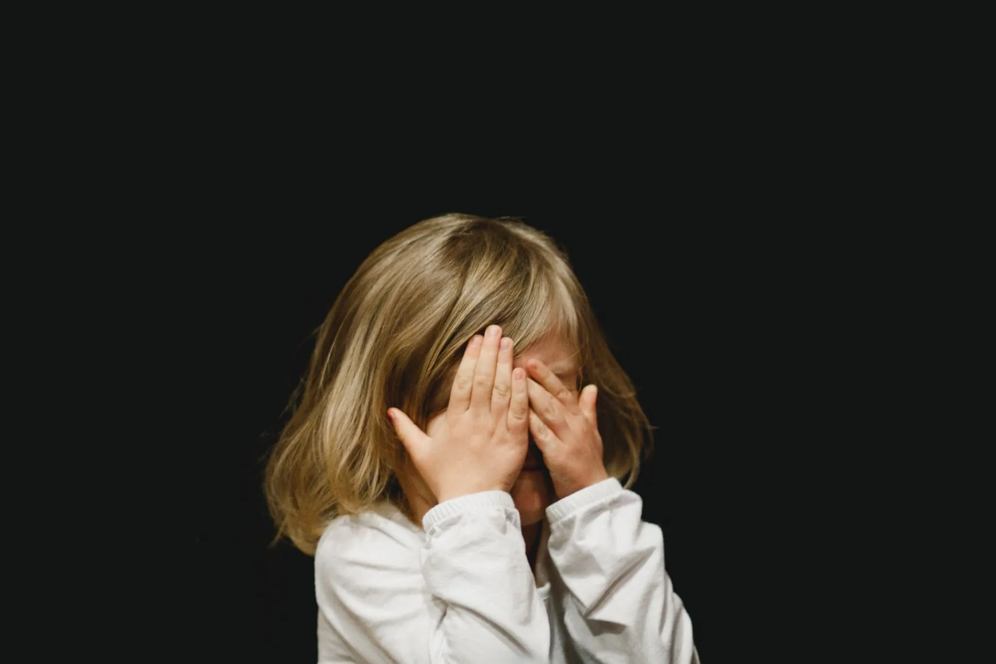 A child hiding behind her hands, nervous to speak in front of a group.