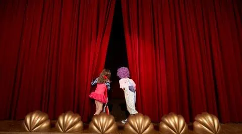 Two children peering behind a theatre curtain