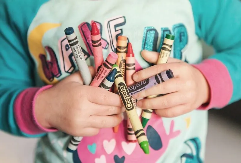 Close up of a child holding a bunch of crayons.