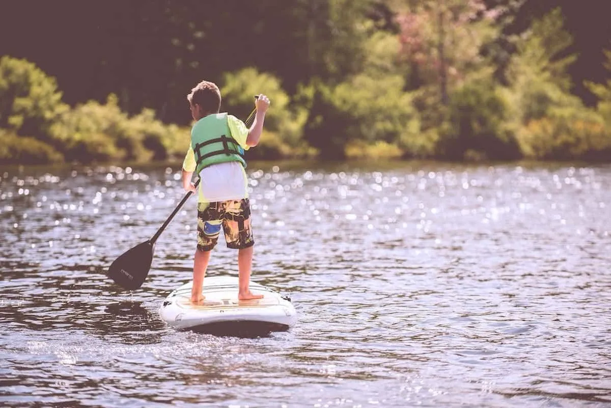 Boy paddleboarding on lake surrounded by trees.