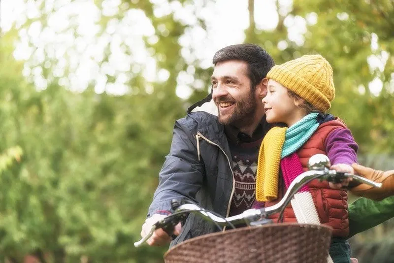 Dad with his daughter sat on the front of his bike in the park.