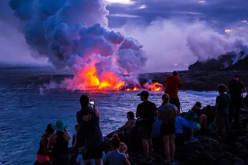 Onlookers watch as lava falls on the water after an eruption.