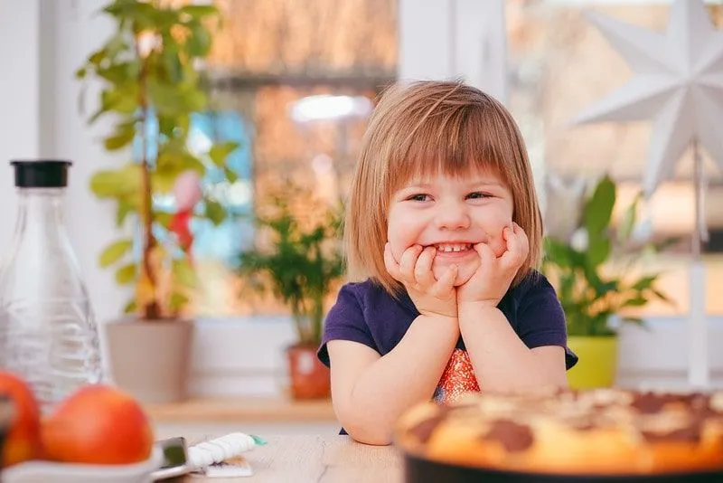 Little girl sat at the kitchen table smiling at cooking jokes.