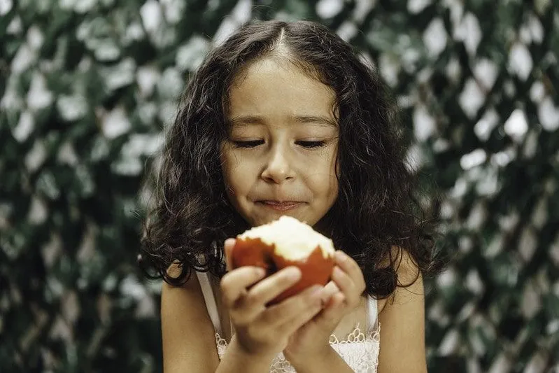 Girl looking at a bitten apple in her hands.