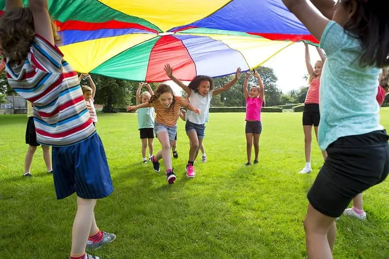 Children outside playing parachute games Two girls are running underneath while the others hold it up.