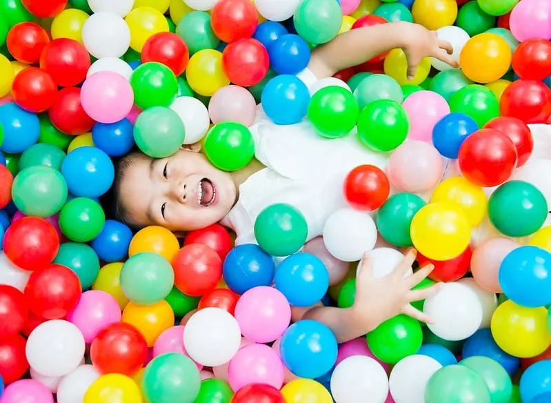 Young boy lying in a ball pit of colourful soft balls.