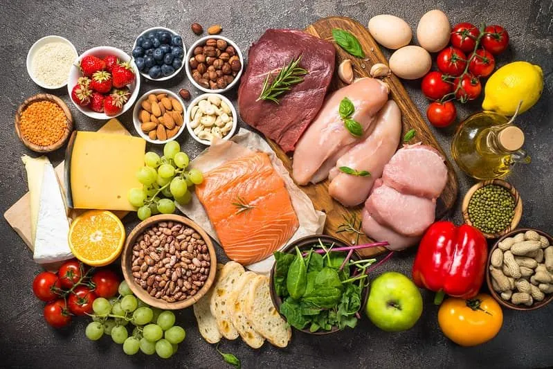 A variety of all kinds of food on a chopping board, including meat, fish, cheese, nuts, eggs, vegetables and oils.