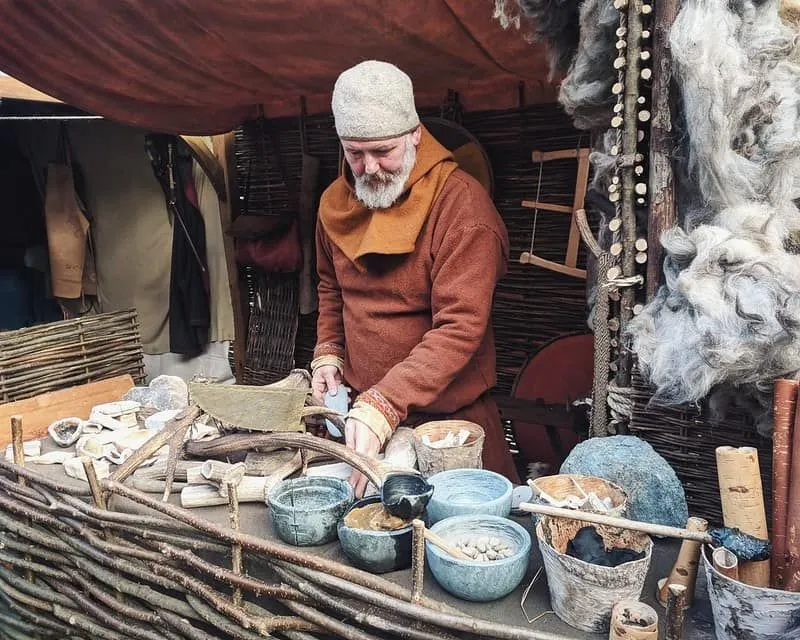 Viking man standing preparing food in clay pots.