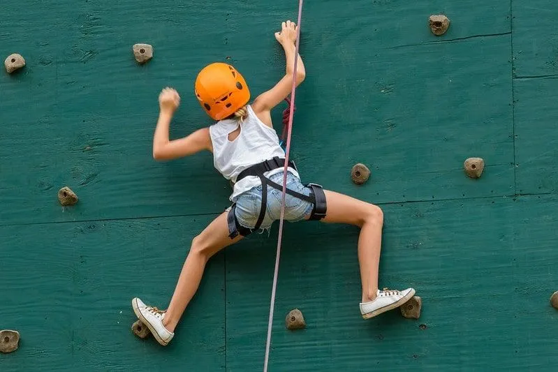 Girl in an orange helmet climbing up a green rock wall.