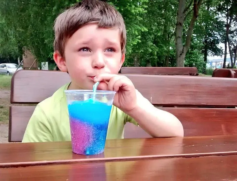Boy sat outside drinking a red and blue slushy.
