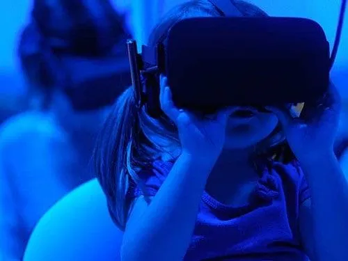 Little girl wearing a VR headset in a blue lit room.