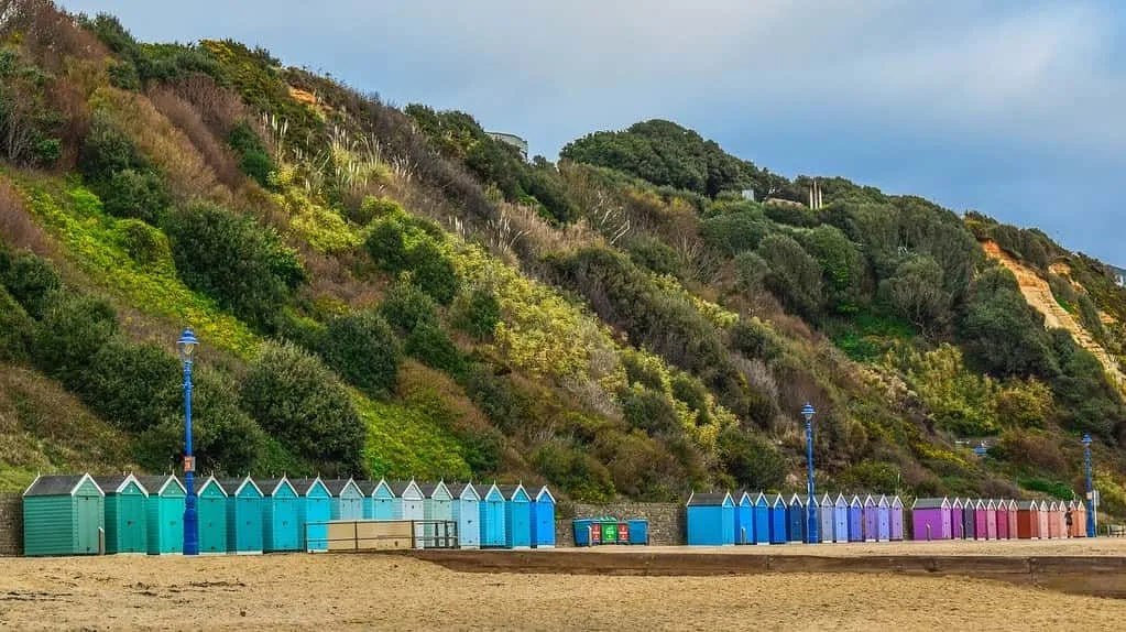 Colourful beach huts lining Bournemouth beach, with green hills behind.