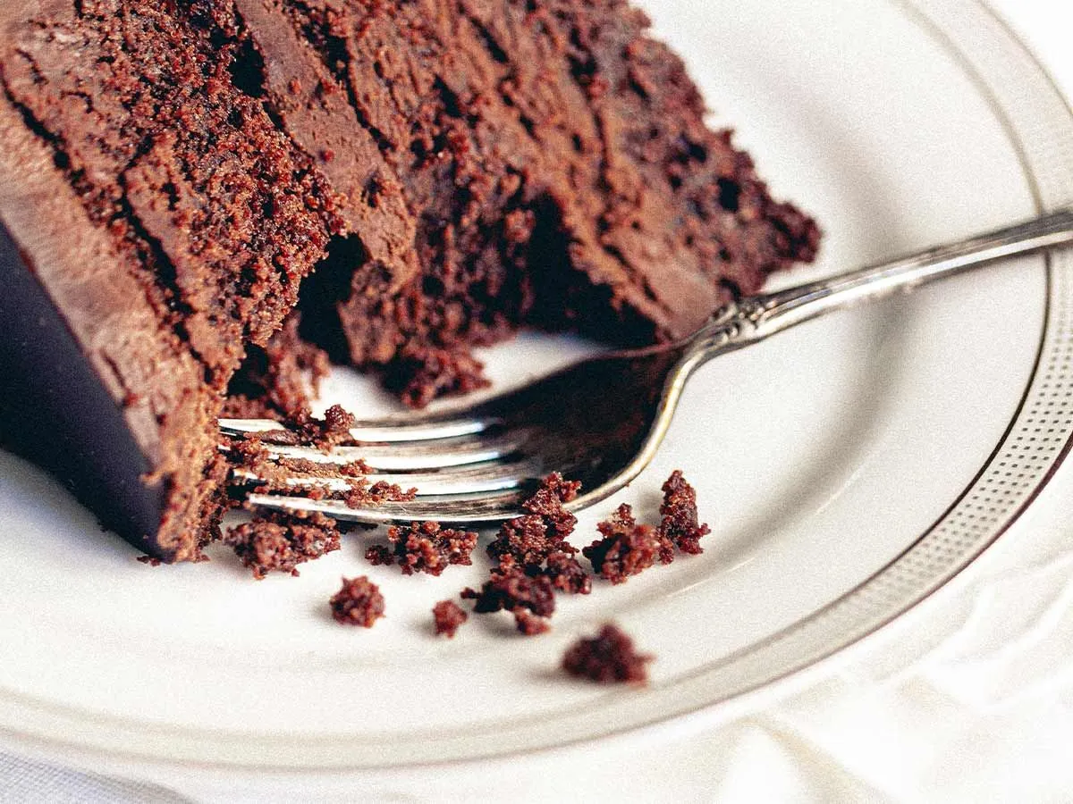 Slice of chocolate cake on a plate with a fork and a bite taken out of it.