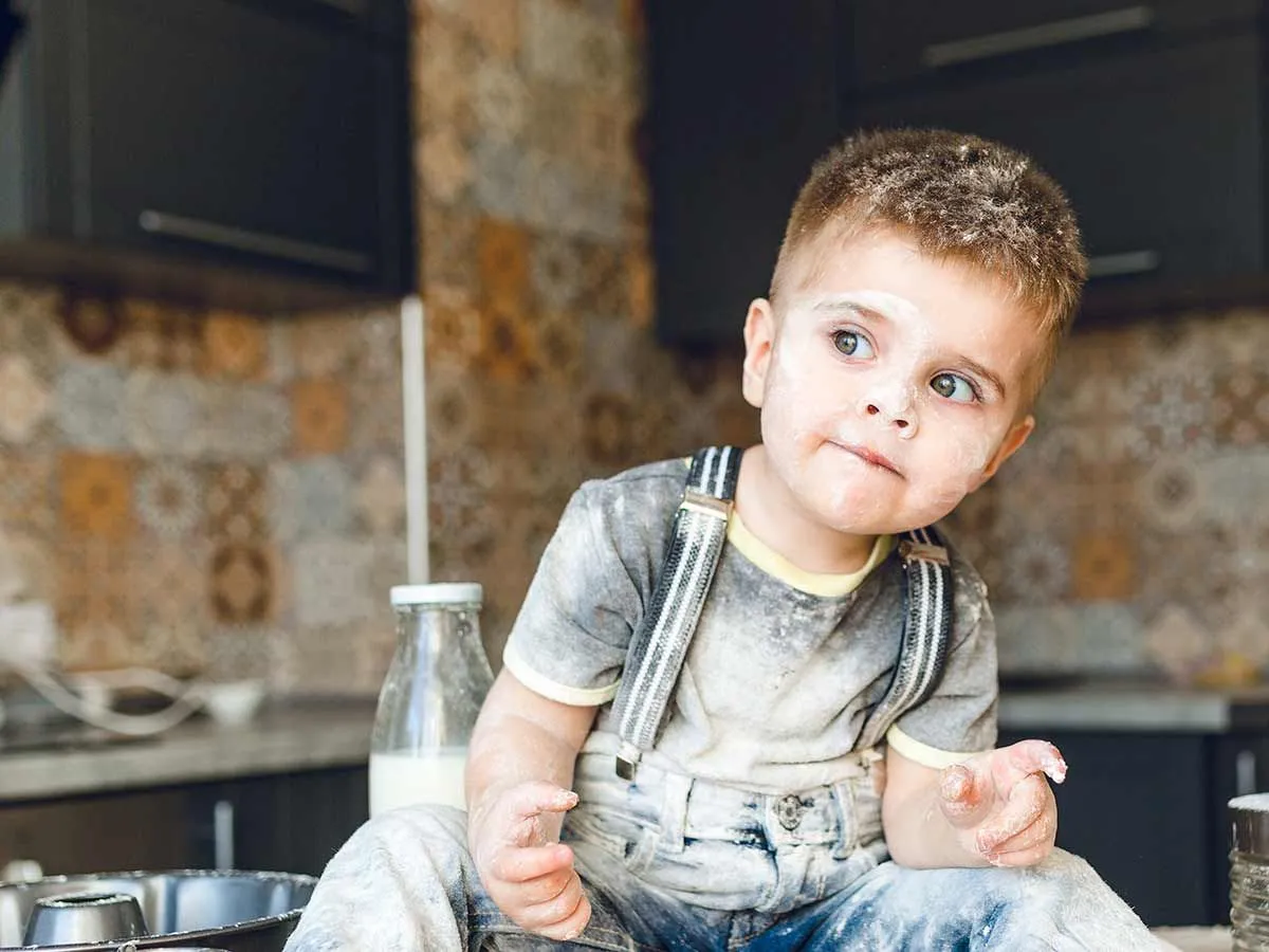Young boy sitting on the kitchen counter covered in flour.