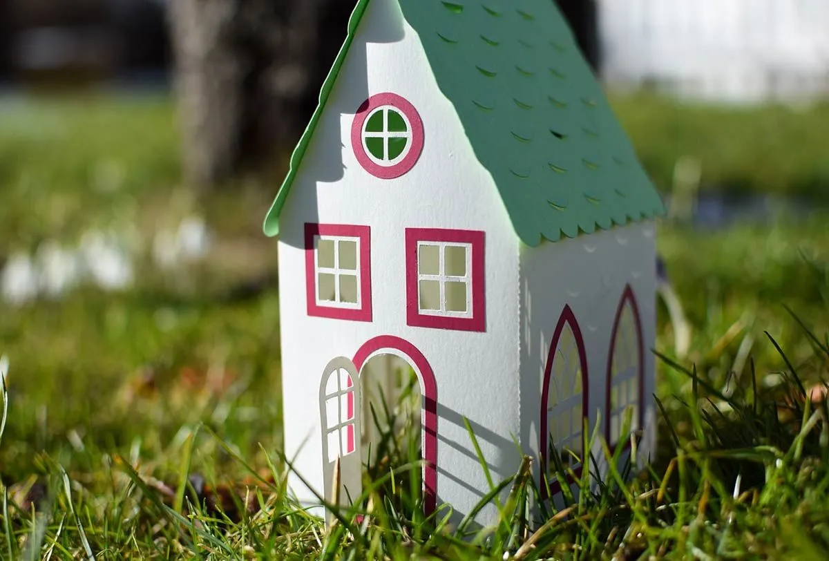 A model house made of card, placed outside on the lawn.