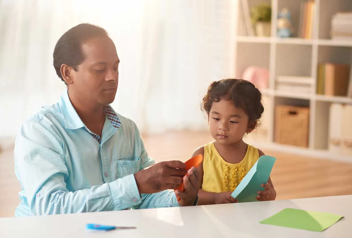 Dad and young daughter sat at the table using paper to make a Viking longboat model.