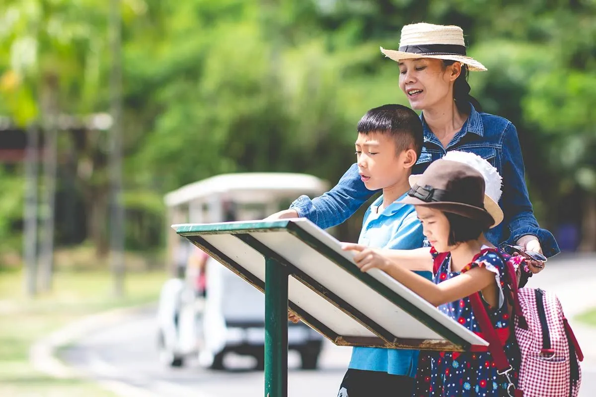 A mother and two children are looking at a country park map on a sunny day, deciding where to go.