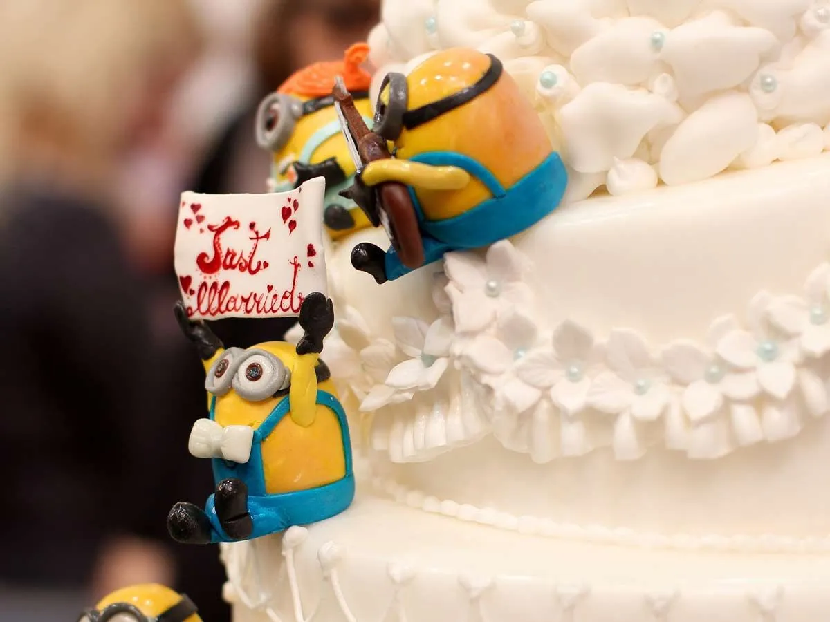 Three fondant minions sitting on the side of a large white cake.