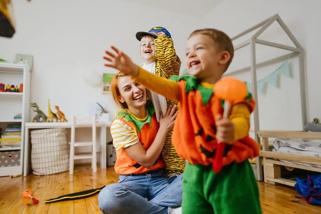 Kids wearing pumpkin costumes running around inside playing with their mum.