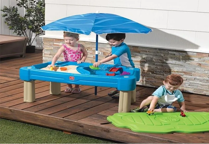 Children playing in the sand and water blue table beside the swimming pool.