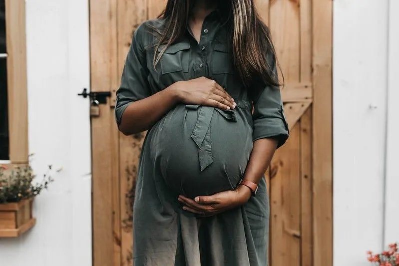 Pregnant woman cradling belly outside. 